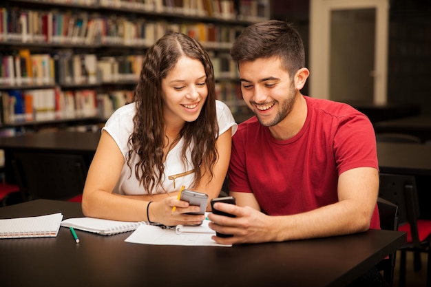 cute-young-couple-college-students-using-their-smartphones-studying-library_662251-1180